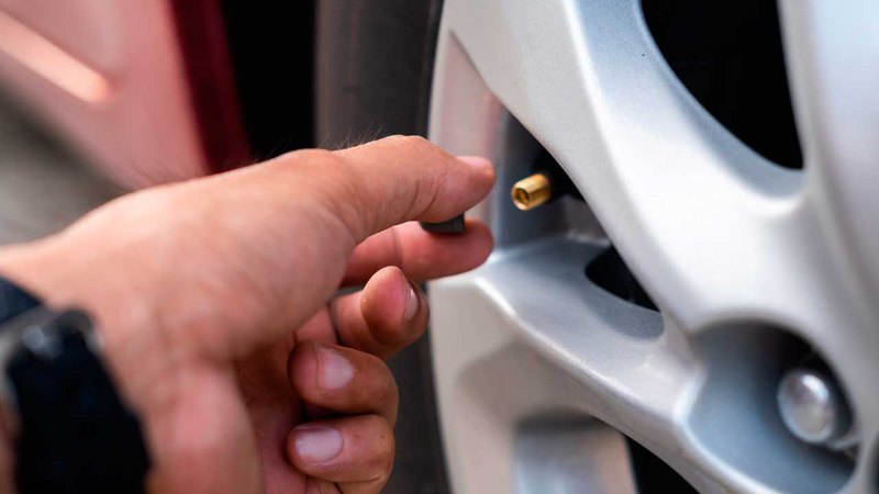 A hand removing the valve stem cap of a tire after deflating max tire pressure for better traction.