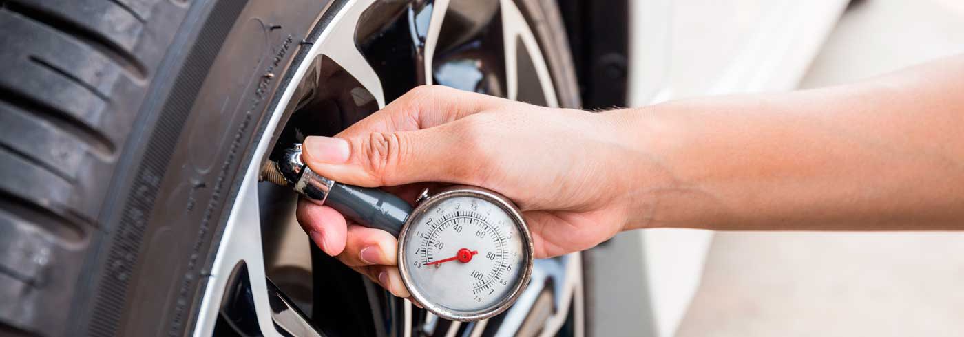 A hand holding a pressure gauge on a valve stem of a car tire to determine the ideal tire pressure