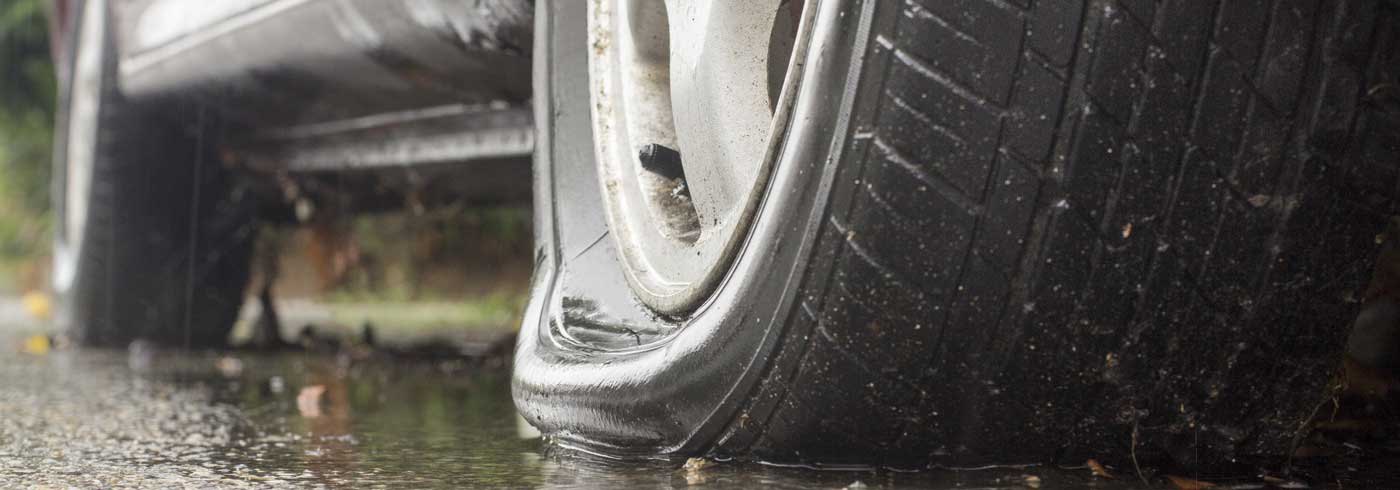 A car with one punctured tire depleted of air. Driving on a flat tire is unsafe and not recommended.
